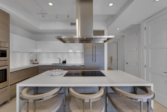 kitchen with a kitchen island, white cabinets, a kitchen bar, island exhaust hood, and black electric stovetop