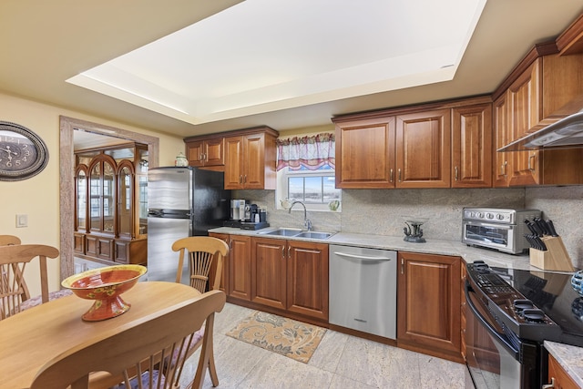 kitchen with appliances with stainless steel finishes, decorative backsplash, sink, light stone counters, and a tray ceiling