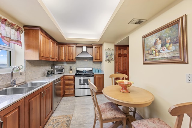 kitchen with sink, light stone counters, appliances with stainless steel finishes, decorative backsplash, and wall chimney range hood