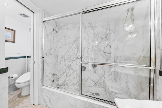 bathroom with toilet, combined bath / shower with glass door, and tile walls