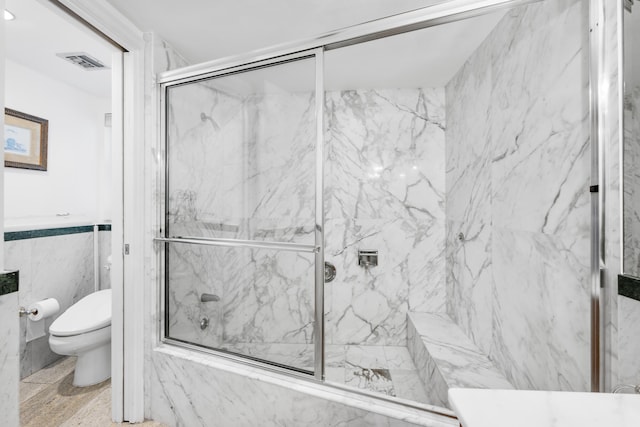 bathroom featuring tile walls, bath / shower combo with glass door, and toilet