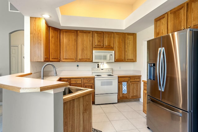 kitchen featuring kitchen peninsula, white appliances, a raised ceiling, sink, and light tile patterned flooring