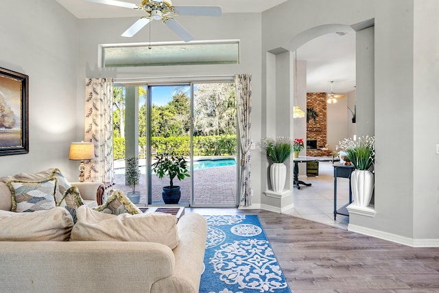 living room with wood-type flooring, a brick fireplace, and ceiling fan