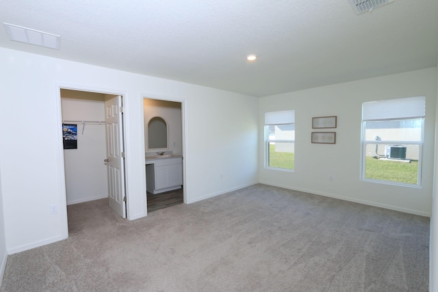 unfurnished bedroom with light carpet, a closet, a spacious closet, and ensuite bath