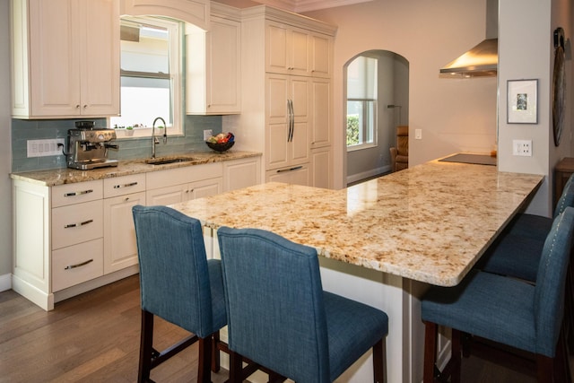 kitchen featuring backsplash, white cabinetry, wall chimney range hood, and a kitchen breakfast bar