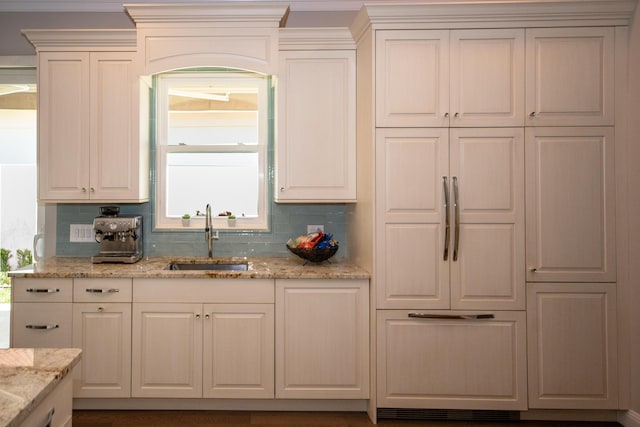 kitchen with light stone counters, sink, backsplash, and white cabinetry