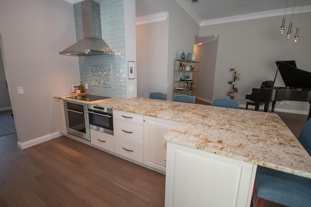 kitchen featuring stainless steel oven, a breakfast bar, wall chimney range hood, and white cabinetry