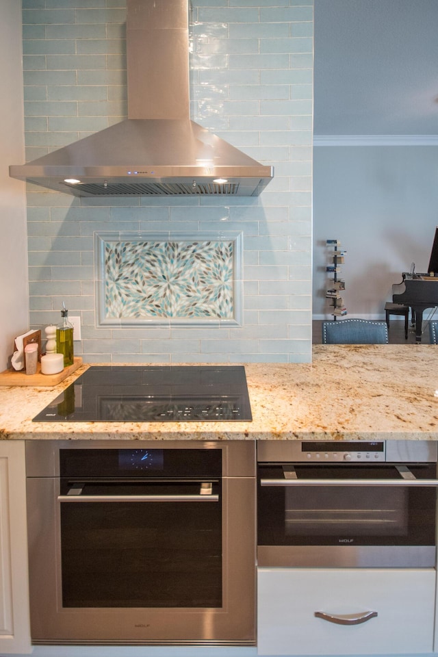 kitchen with black electric stovetop, stainless steel oven, light stone counters, and wall chimney range hood