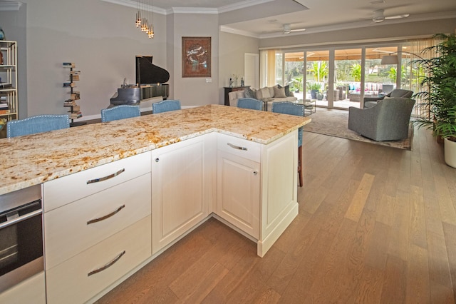 kitchen featuring white cabinetry, ceiling fan, light wood-type flooring, light stone countertops, and ornamental molding