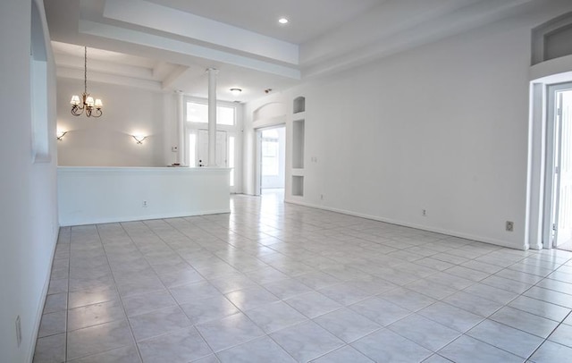 tiled spare room with a tray ceiling, a high ceiling, and an inviting chandelier