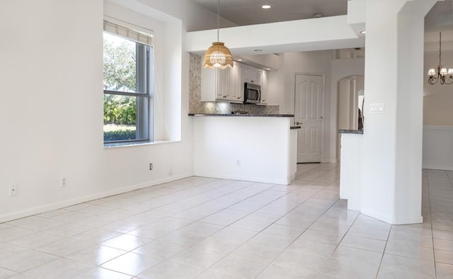 interior space with tasteful backsplash, decorative light fixtures, a notable chandelier, white cabinetry, and light tile patterned flooring