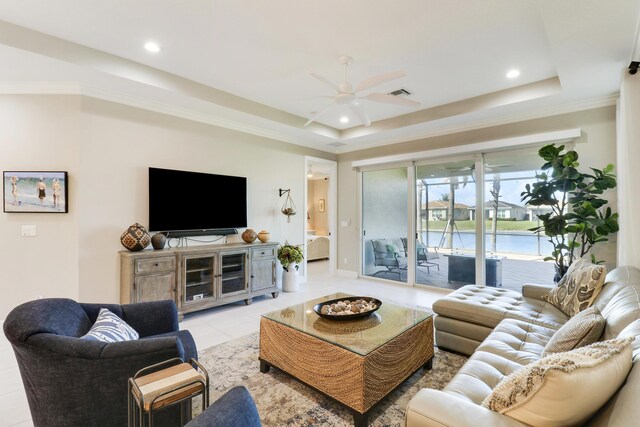 living room with light tile patterned flooring, a tray ceiling, ceiling fan, and a water view