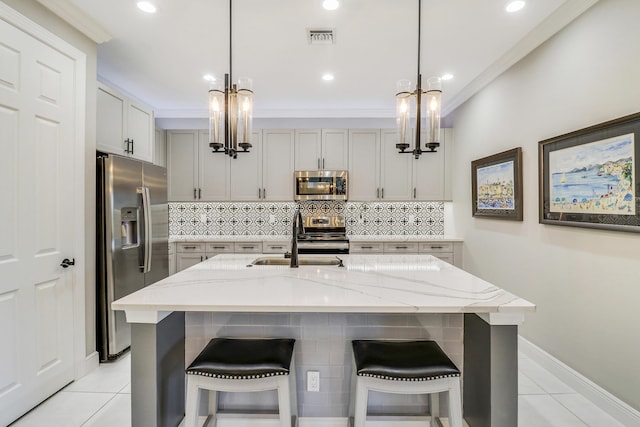 kitchen with light stone countertops, sink, stainless steel appliances, an island with sink, and gray cabinets