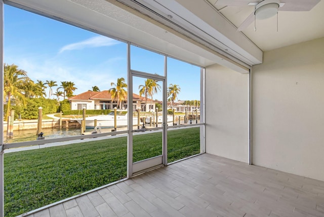 unfurnished sunroom featuring ceiling fan, a water view, and a wealth of natural light