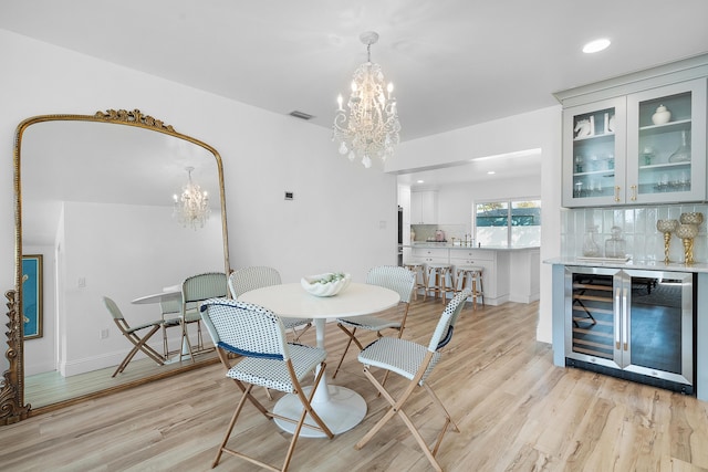 dining area with wine cooler, an inviting chandelier, light hardwood / wood-style flooring, and bar area