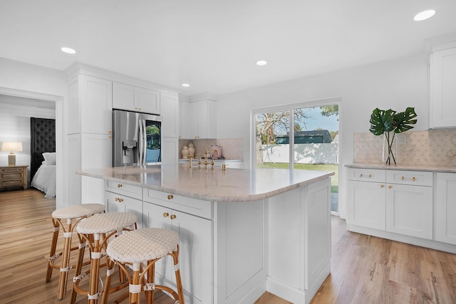 kitchen with a kitchen bar, light hardwood / wood-style flooring, stainless steel refrigerator with ice dispenser, light stone counters, and white cabinets