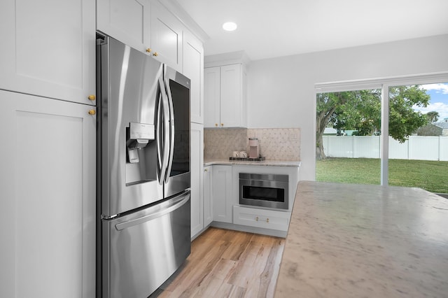 kitchen with decorative backsplash, light wood-type flooring, stainless steel fridge with ice dispenser, and white cabinets