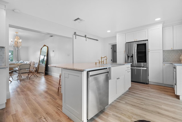 kitchen with a center island with sink, stainless steel appliances, white cabinets, a barn door, and sink