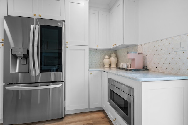 kitchen with tasteful backsplash, stainless steel appliances, white cabinetry, and light wood-type flooring