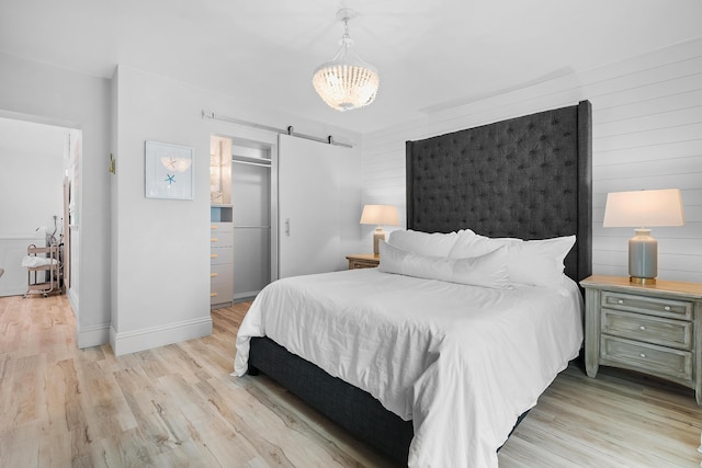 bedroom featuring light wood-type flooring, a closet, a chandelier, and a barn door