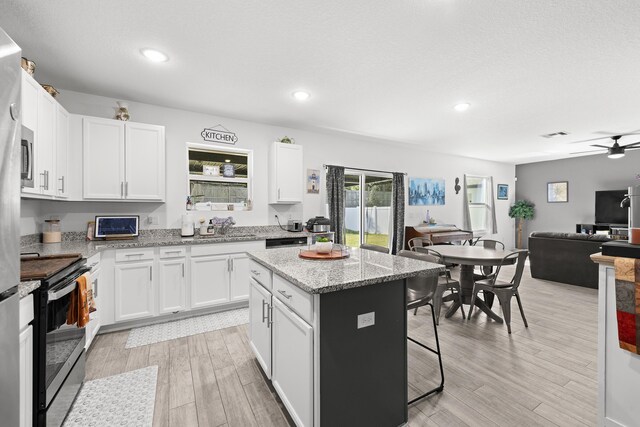 kitchen featuring white cabinets, a center island, ceiling fan, and electric range