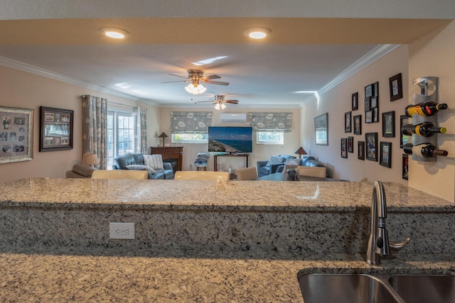 kitchen with light stone countertops, ceiling fan, crown molding, and sink