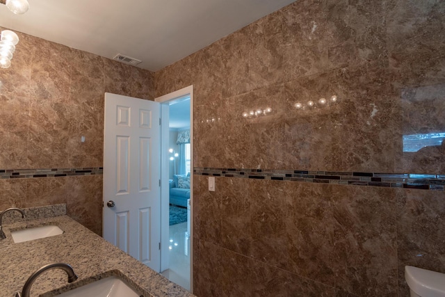 bathroom featuring toilet, tile walls, and sink