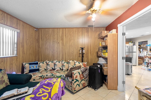 living room with wooden walls, light tile patterned flooring, a textured ceiling, and ceiling fan