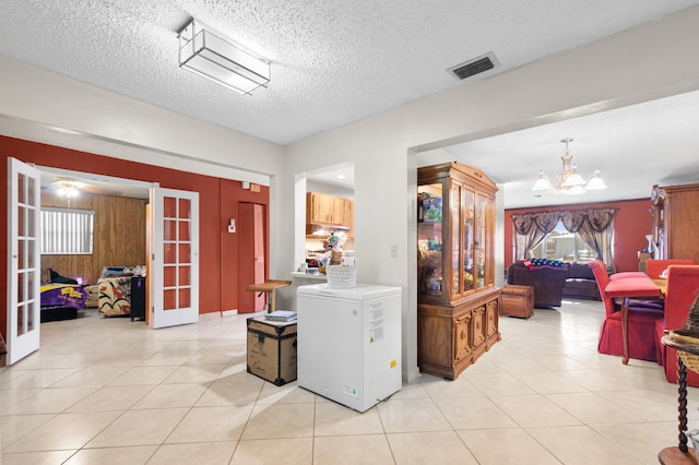 hallway with french doors, light tile patterned flooring, a textured ceiling, and an inviting chandelier