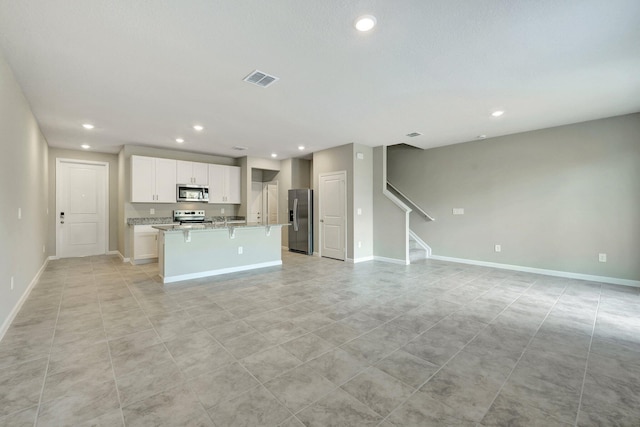 kitchen featuring white cabinetry, a center island with sink, light stone countertops, and appliances with stainless steel finishes