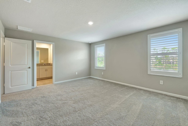 unfurnished bedroom featuring connected bathroom, light carpet, and a textured ceiling