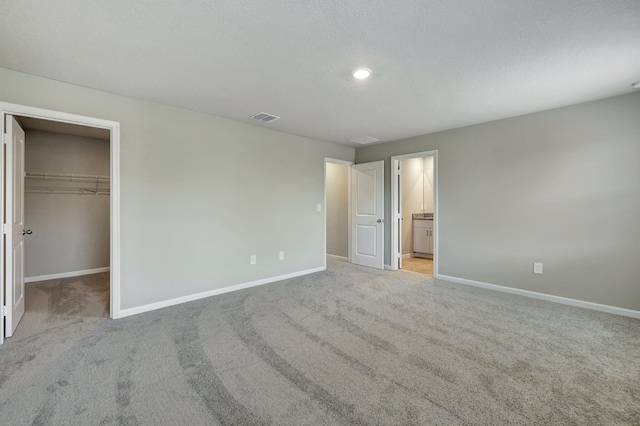 unfurnished bedroom featuring connected bathroom, a spacious closet, a textured ceiling, a closet, and light colored carpet