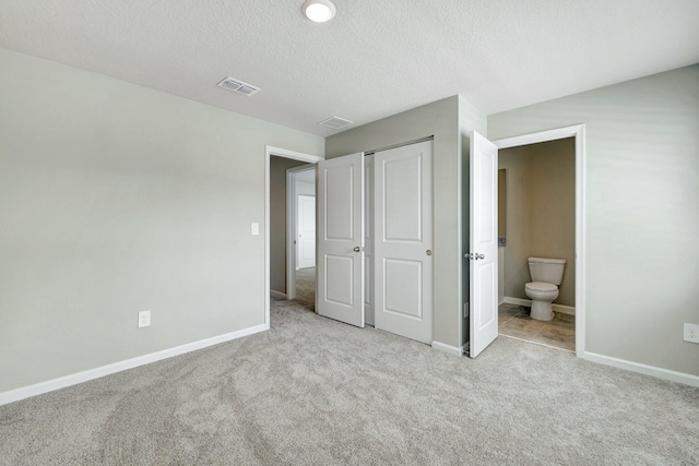 unfurnished bedroom with ensuite bathroom, light carpet, a textured ceiling, and a closet