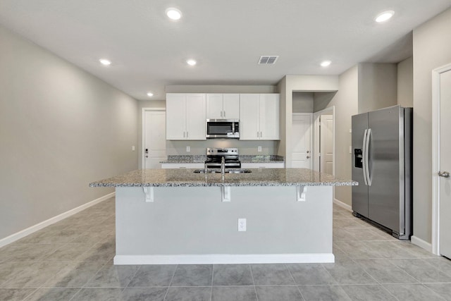 kitchen featuring white cabinets, appliances with stainless steel finishes, a kitchen island with sink, and dark stone countertops