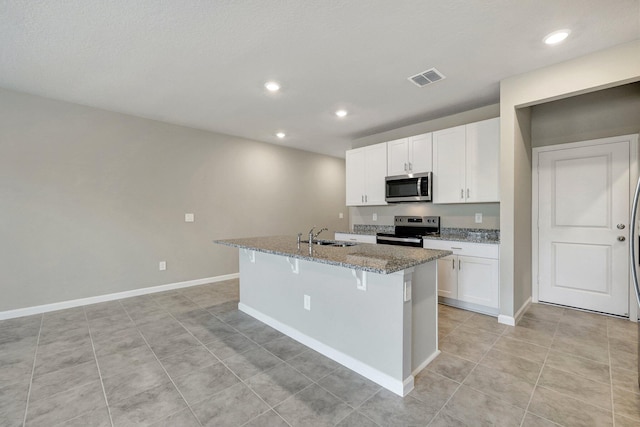 kitchen featuring stone counters, appliances with stainless steel finishes, an island with sink, a breakfast bar area, and white cabinets