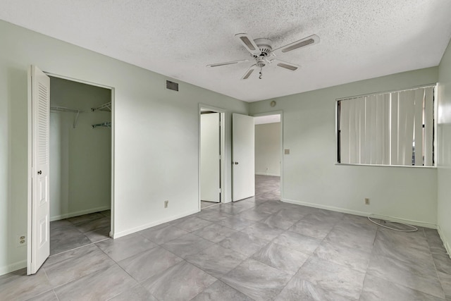 unfurnished bedroom featuring ceiling fan, a spacious closet, a textured ceiling, and a closet