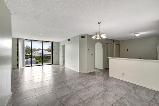 unfurnished room with arched walkways, a notable chandelier, a textured ceiling, a wall of windows, and baseboards