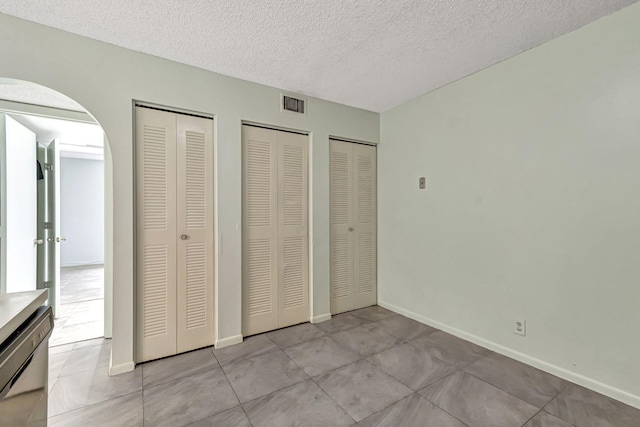 unfurnished bedroom featuring light tile patterned floors, a textured ceiling, and two closets