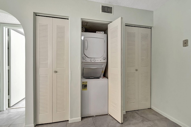 laundry room featuring a textured ceiling, light tile patterned floors, and stacked washer / dryer