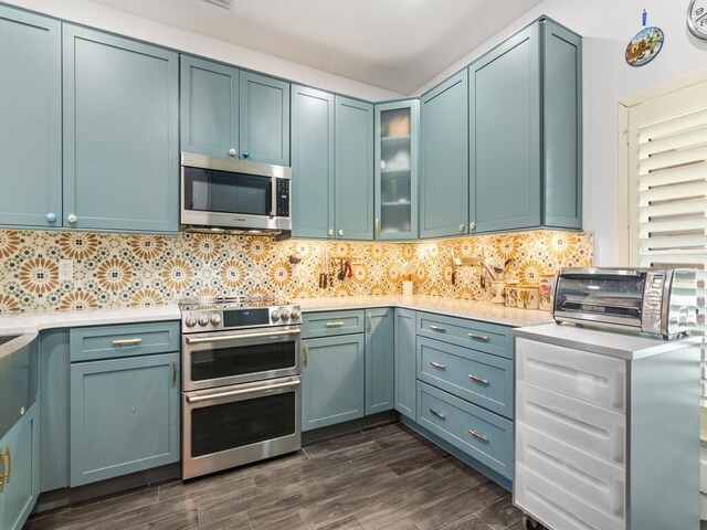 kitchen with appliances with stainless steel finishes, tasteful backsplash, sink, dark hardwood / wood-style floors, and blue cabinets