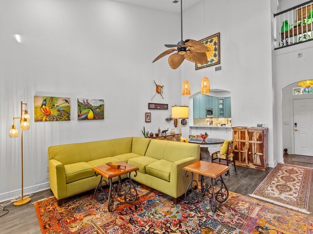 living room featuring ceiling fan, hardwood / wood-style floors, and a towering ceiling