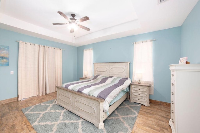 bedroom featuring a tray ceiling, ceiling fan, and light hardwood / wood-style flooring