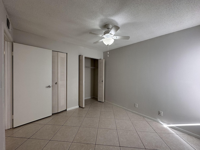 unfurnished bedroom with two closets, a textured ceiling, ceiling fan, and light tile patterned floors