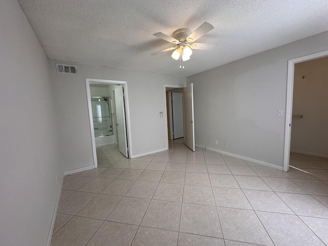 unfurnished bedroom featuring ceiling fan, connected bathroom, light tile patterned floors, and a textured ceiling