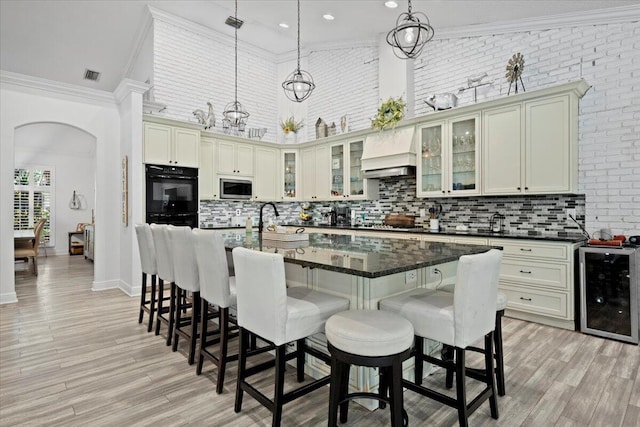 kitchen with custom exhaust hood, hanging light fixtures, a kitchen island with sink, and cream cabinetry