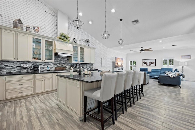 kitchen with an island with sink, pendant lighting, light wood-type flooring, and cream cabinetry