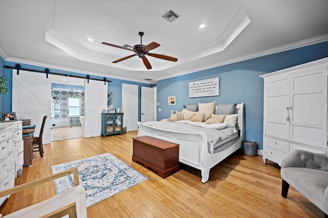 bedroom featuring a raised ceiling, ornamental molding, a barn door, and light hardwood / wood-style floors