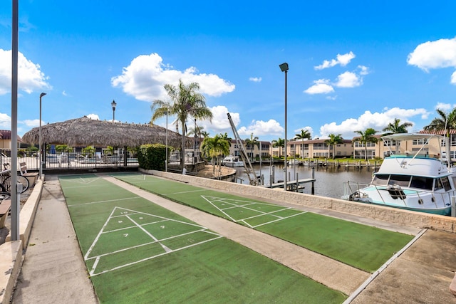 view of property's community with a dock, shuffleboard, fence, and a water view