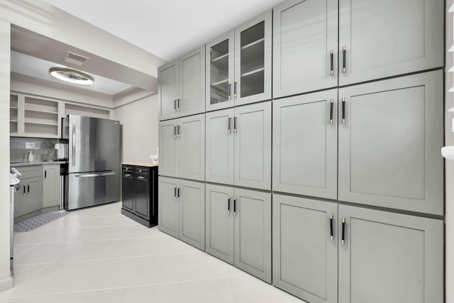 kitchen featuring light tile patterned floors, visible vents, freestanding refrigerator, light countertops, and glass insert cabinets