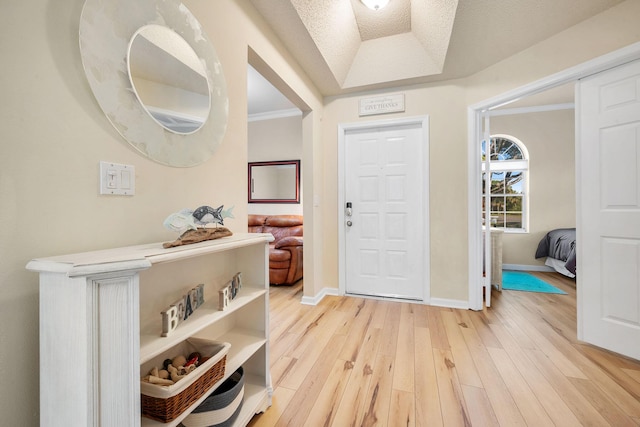 entrance foyer featuring light wood-type flooring, a tray ceiling, baseboards, and crown molding